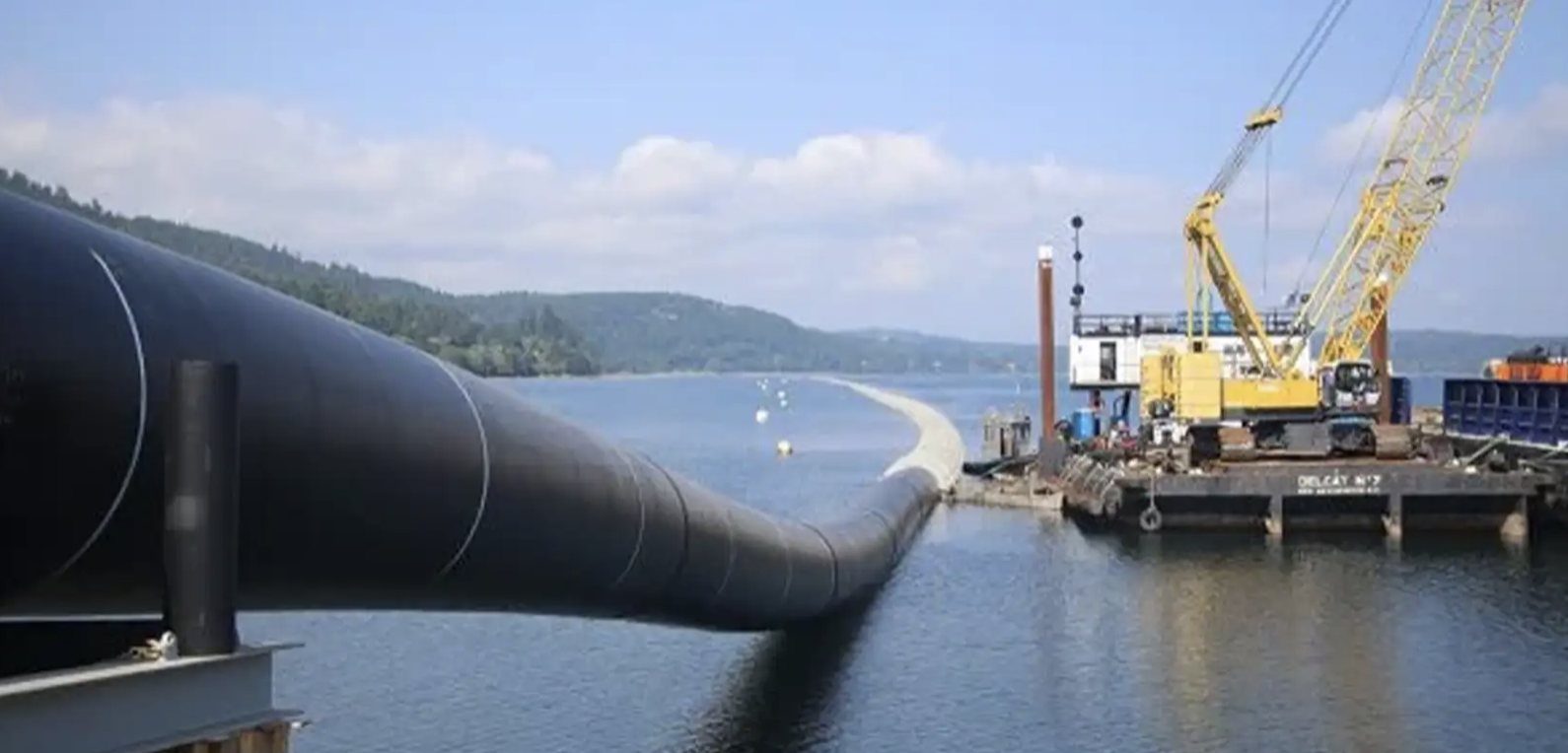 Large black pipe running out over water toward a crane barge