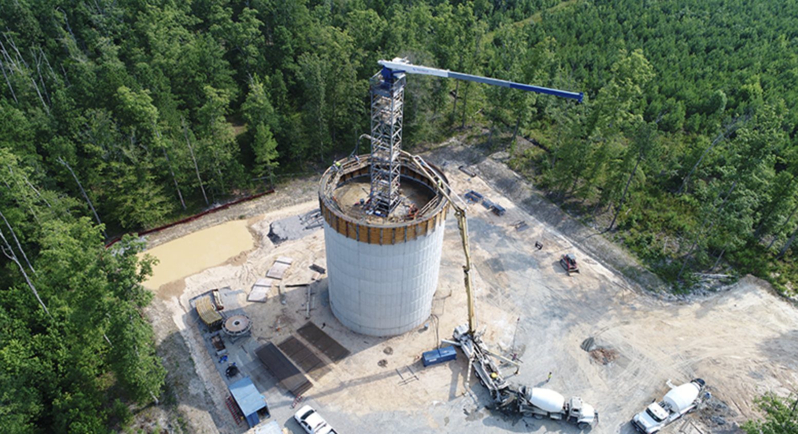 Aerial view of a concrete tank pedestal under construction with a crane and concrete trucks on site